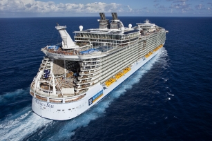 Aerial view of the Allure of the Seas ship as it sails away from the camera with the royal caribbean colours against it. 