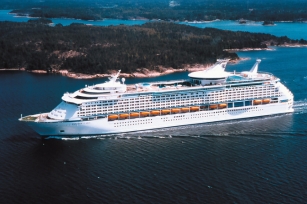 aerial image of the cruise ship Explorer of the Seas, cruising throught the blue/green seas with the gorgeous forested land behind the cruise ship 